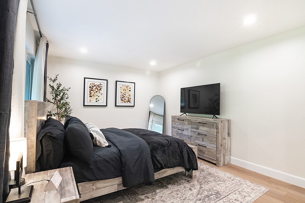A bedroom with a made bed, a wood dresser with a TV and a full-length mirror