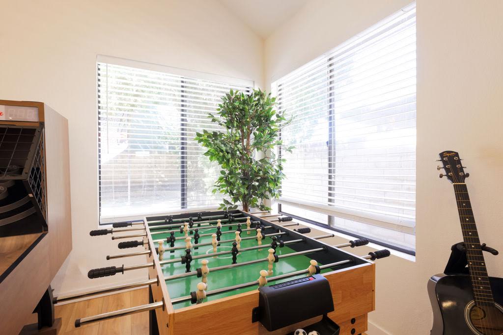 A foosball table by a bright corner window in the Home B game room
