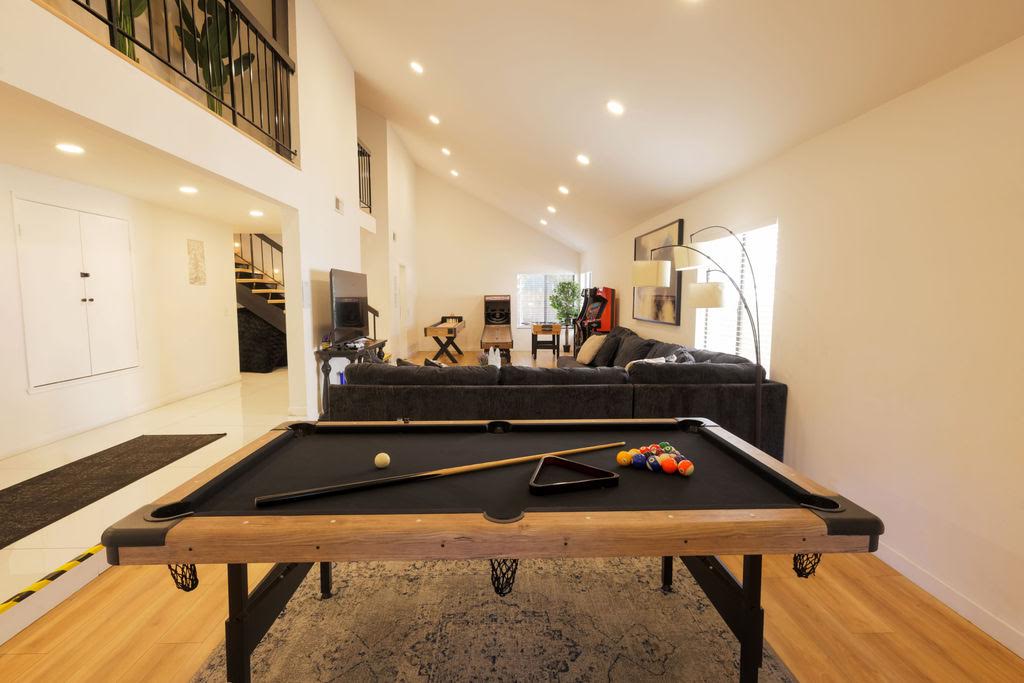 A pool table in the Home B game room, with a sectional sofa and arcade machines behind it