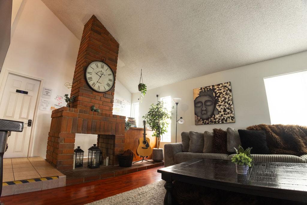 The Home B living room, with a brick fireplace, a large wall clock and an acoustic guitar beside a gray sectional