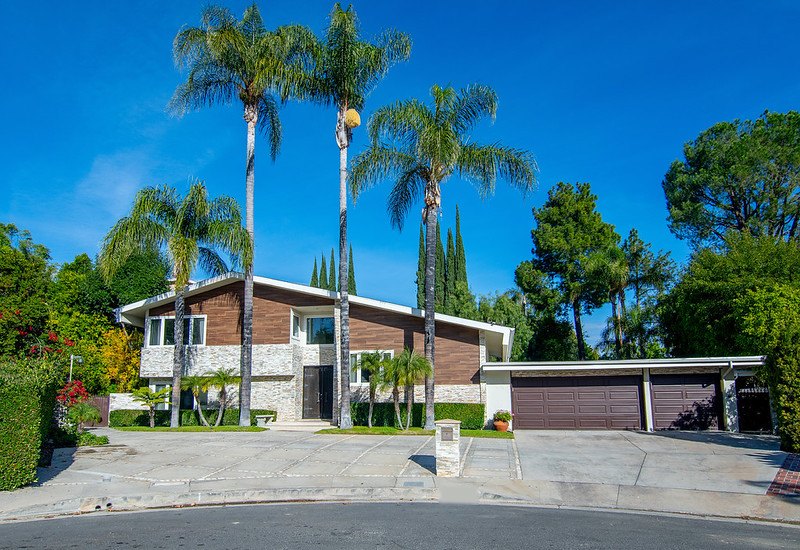 The front of Serenity Moon Recovery in Winnetka: a two-story mid-century home with stone and wood siding behind tall palm trees